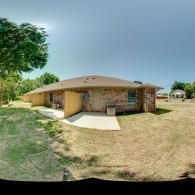 Single-story brick house with tan roof and concrete walkway in a dry yard, under a cloudy sky