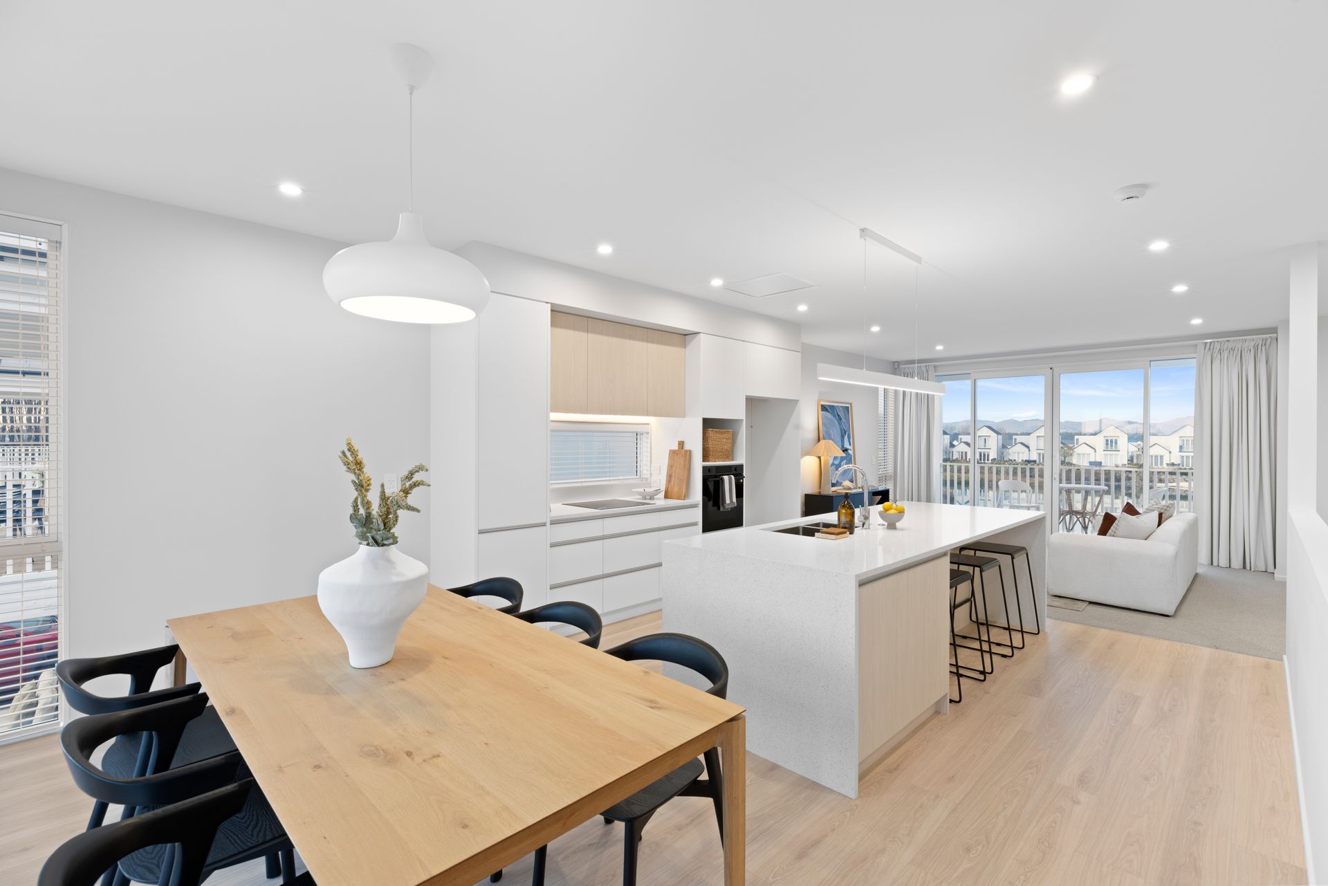 Modern open-plan kitchen and dining area with light wood flooring, white cabinetry, and a large island.