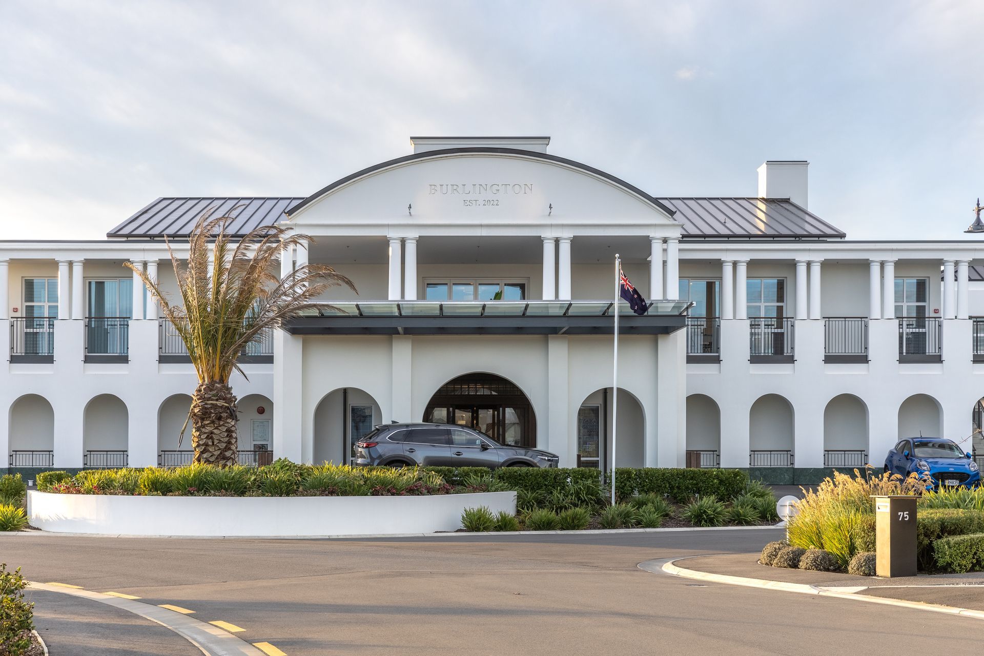 White building with arched entrance and black SUV parked under a glass awning.