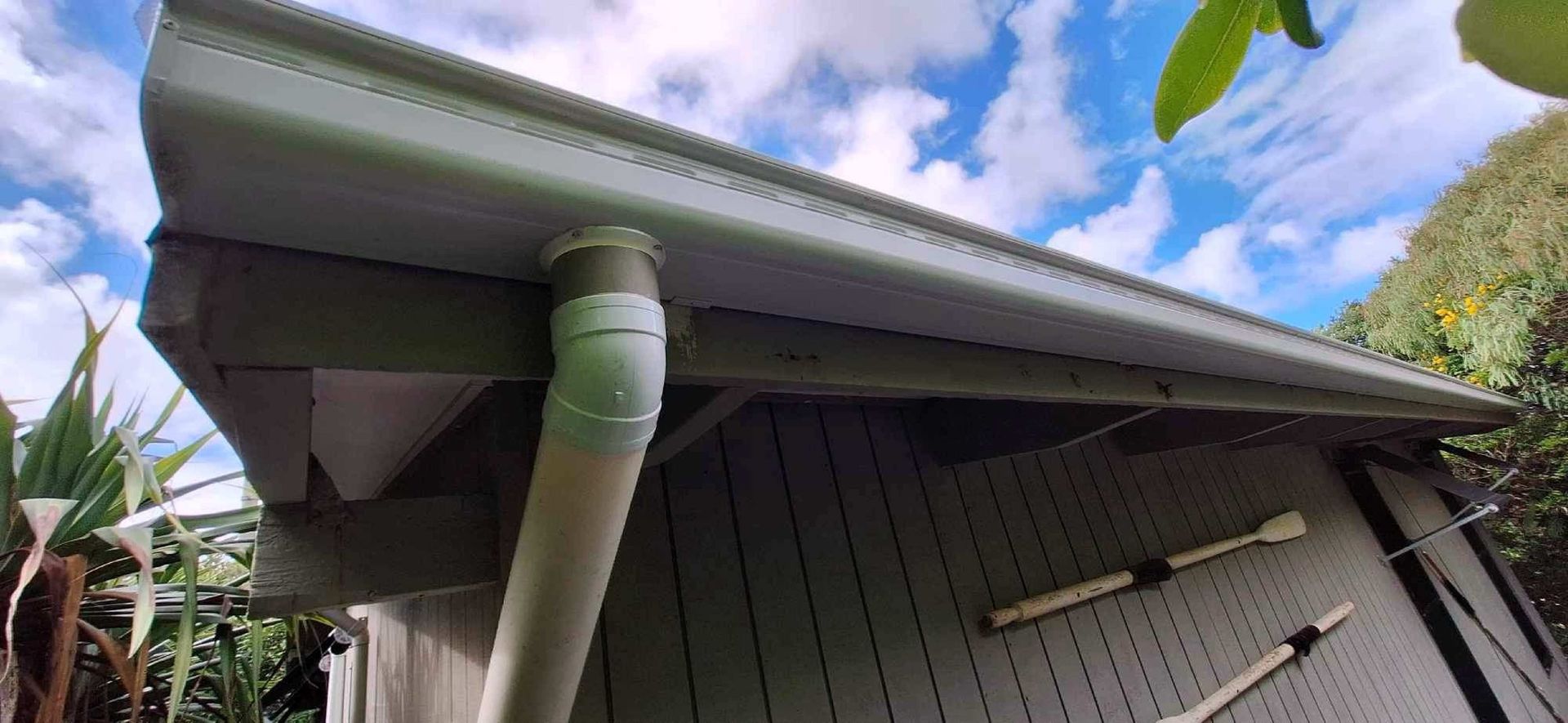 A Person Is Cleaning A Gutter Of Leaves From A Roof — Coastal Roof & Gutter Services In Coolum Beach, QLD