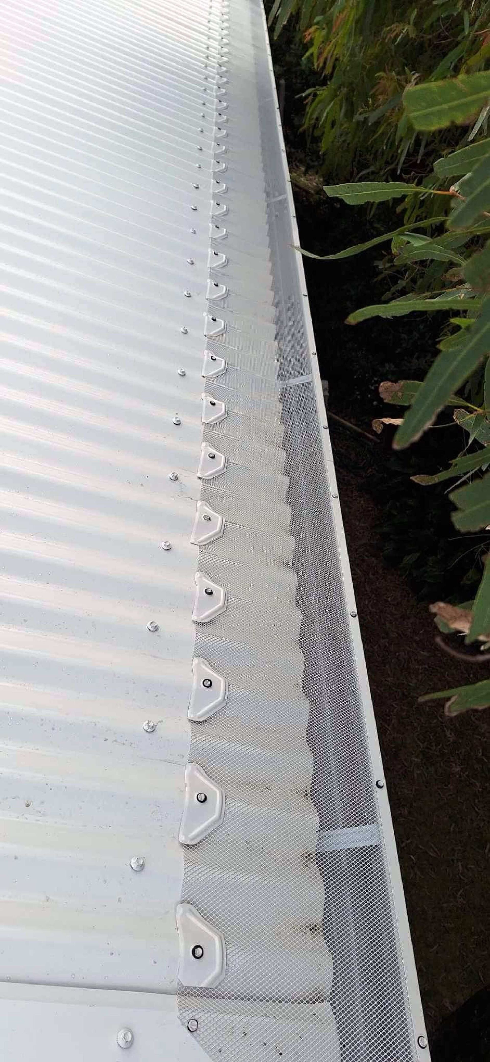 A Man Is Installing A Gutter On The Side Of A Brick Building — Coastal Roof & Gutter Services In Coolum Beach, QLD