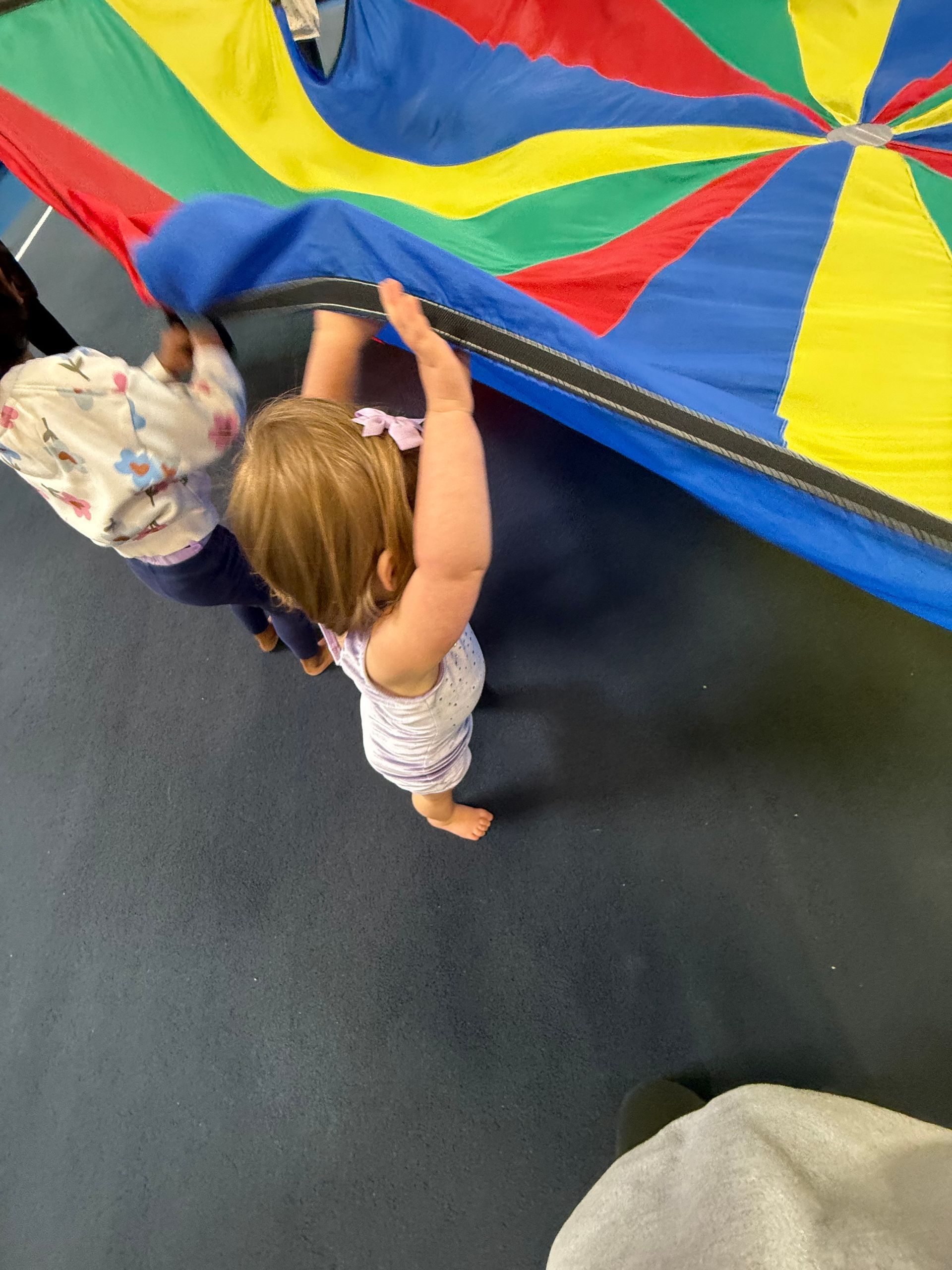 A little girl is playing with a colorful parachute