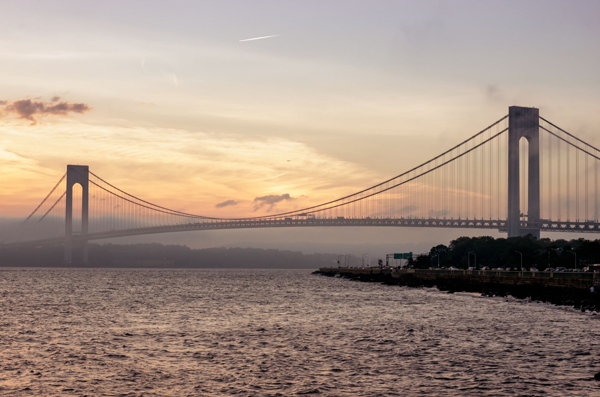 Suspension bridge over water at sunset, with warm sky and distant shoreline