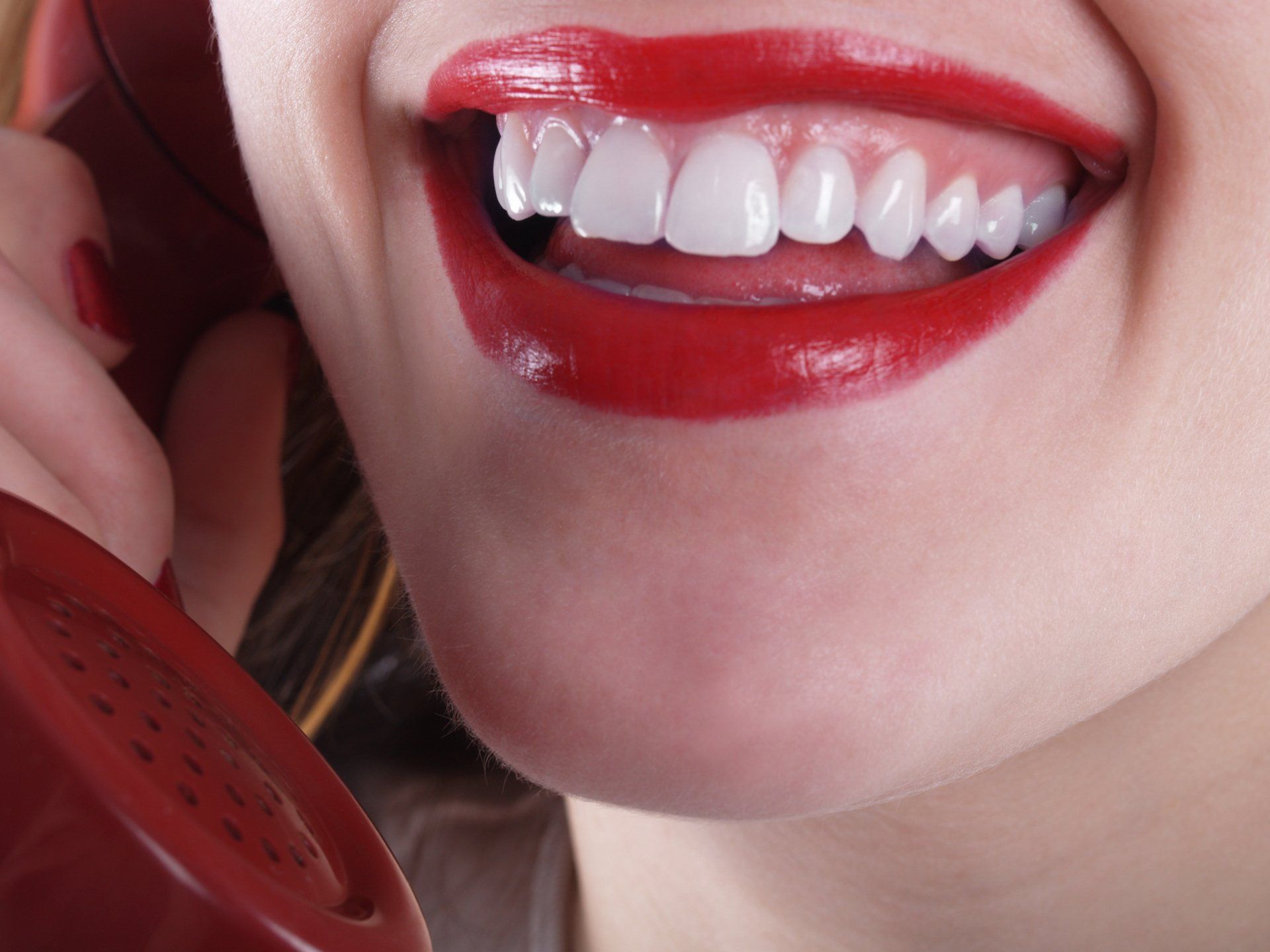 A woman with red lipstick is talking on a red phone