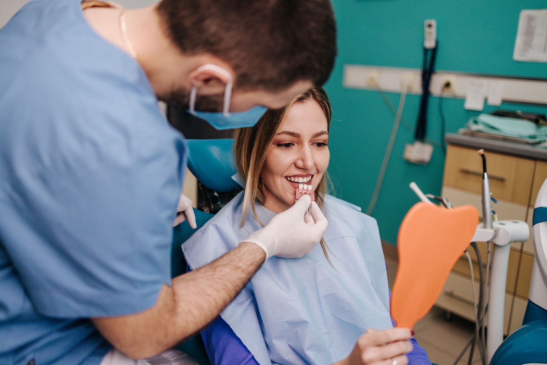 Dentist examines a smiling patient in a dental chair, using a mirror and tools in a clinic.