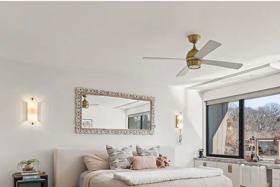 Bright minimalist bedroom with a white bed, decorative mirror, wall sconces, and a window seat by a large window.