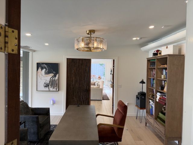 Modern dining room with long table, red chair, wood cabinets, and a doorway to a bright kitchen