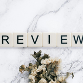 “REVIEW” spelled with letter tiles on a white marble background, with dried flowers below