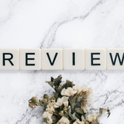 “REVIEW” spelled with letter tiles on a white marble background, with dried flowers below