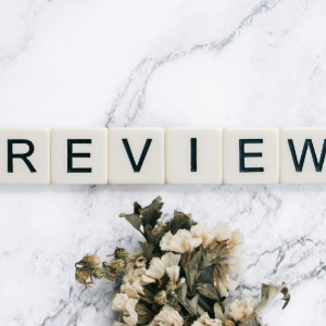 “REVIEW” spelled with letter tiles on a white marble background, with dried flowers below