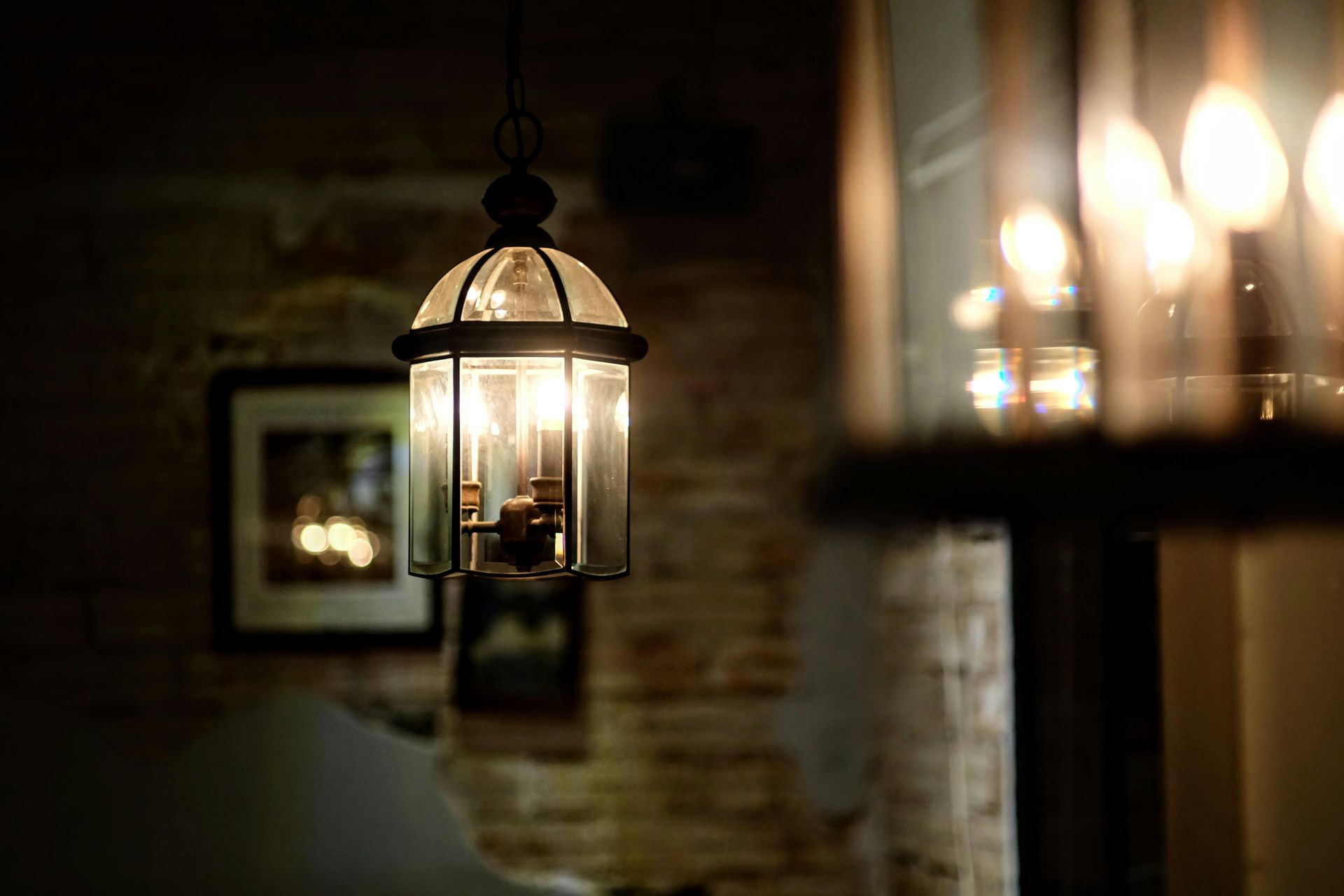 Warm hanging lanterns glow in a dim room with brick walls and blurred candles in the background
