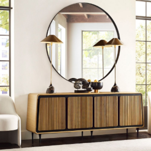 Oval wooden wall mirror above a shelf with a plant, candle, and jewelry stand