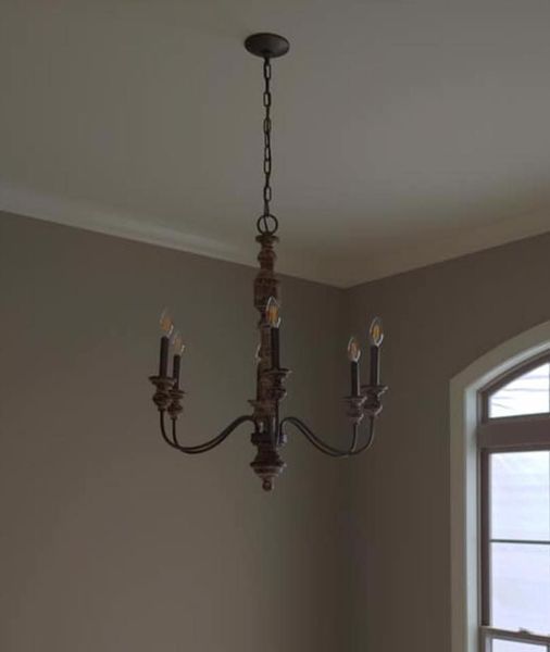 Dark metal chandelier with candle-style bulbs hanging in a beige room near an arched window