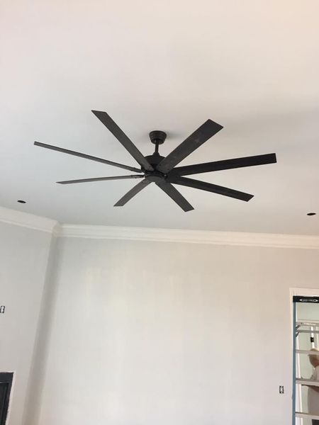 Modern black ceiling fan with long blades on a white ceiling in a bright room