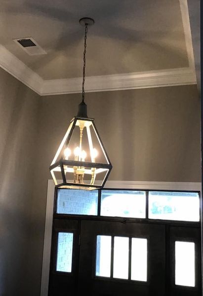 Black pendant light hanging from a ceiling above a front door with sidelights and transom windows