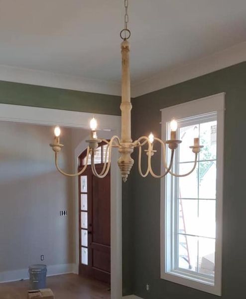 Brass chandelier hanging in a room with green walls, white trim, and a window letting in daylight