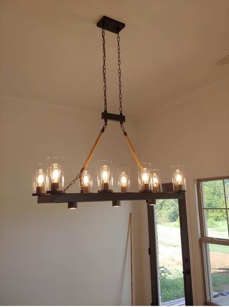 Modern black chandelier with lit bulbs hanging from the ceiling in a room near a window.