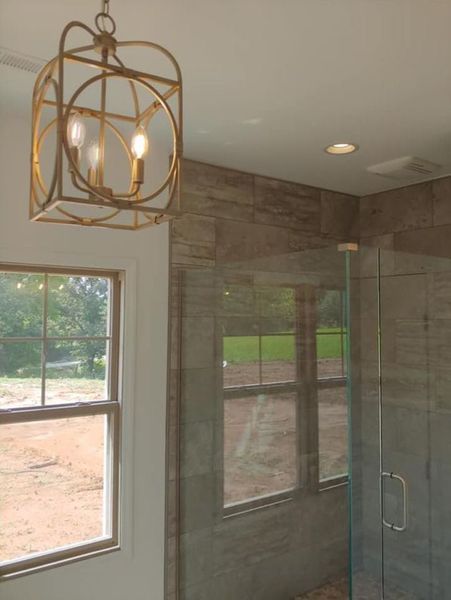 Bathroom with gold pendant light, marble tile walls, windows, and a glass shower door.
