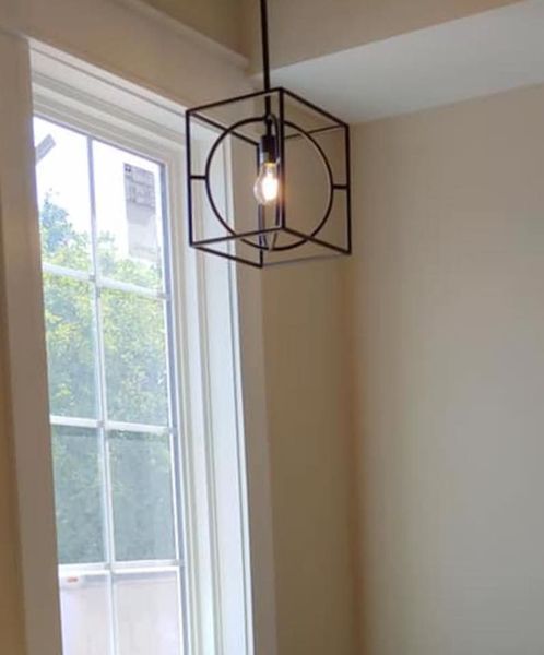 Geometric black pendant light hanging beside a sunlit window in a beige room