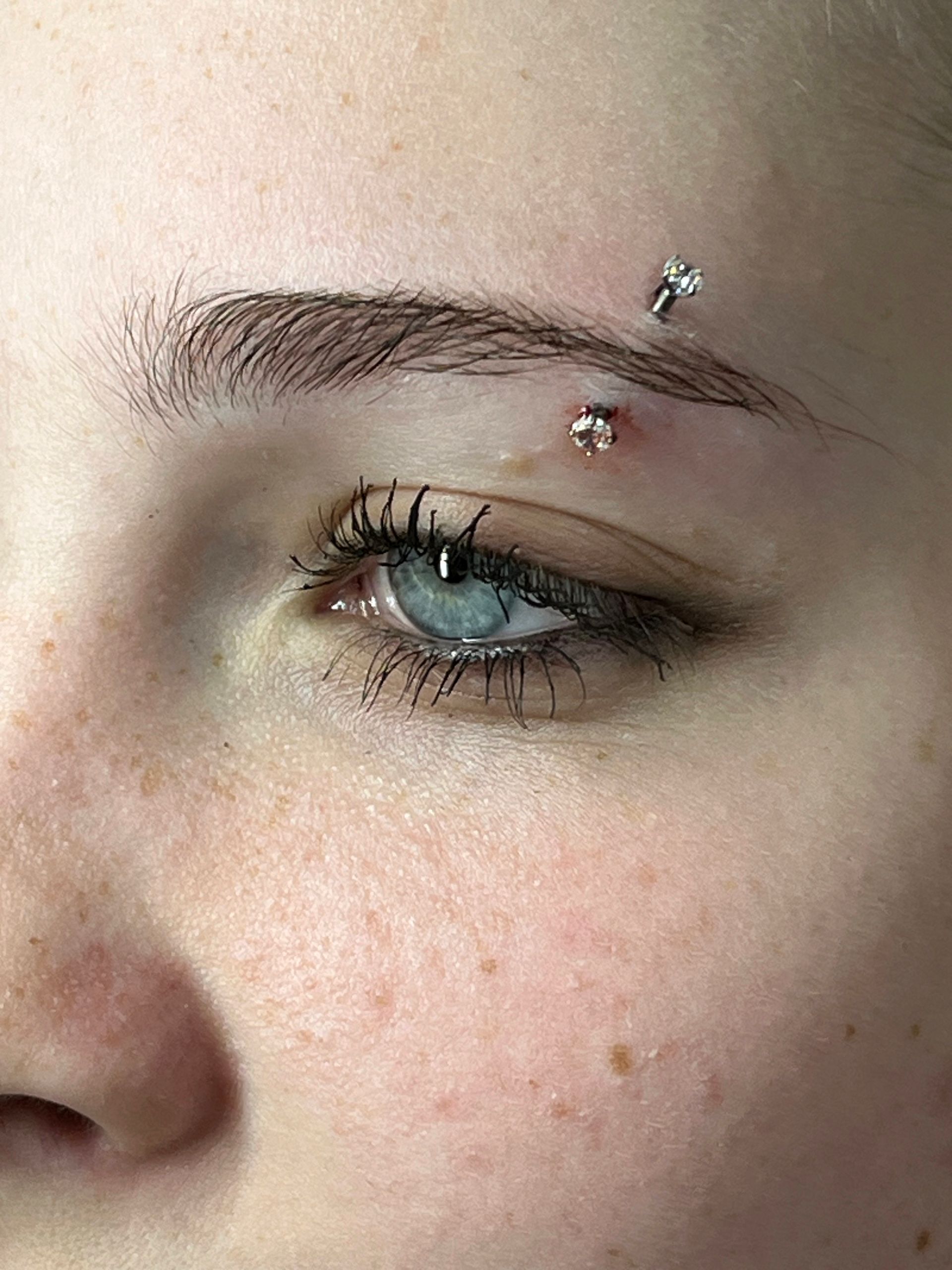 Een close-up van een wenkbrauw met een zilveren staafpiercing met transparante steentjes aan beide uiteinden.