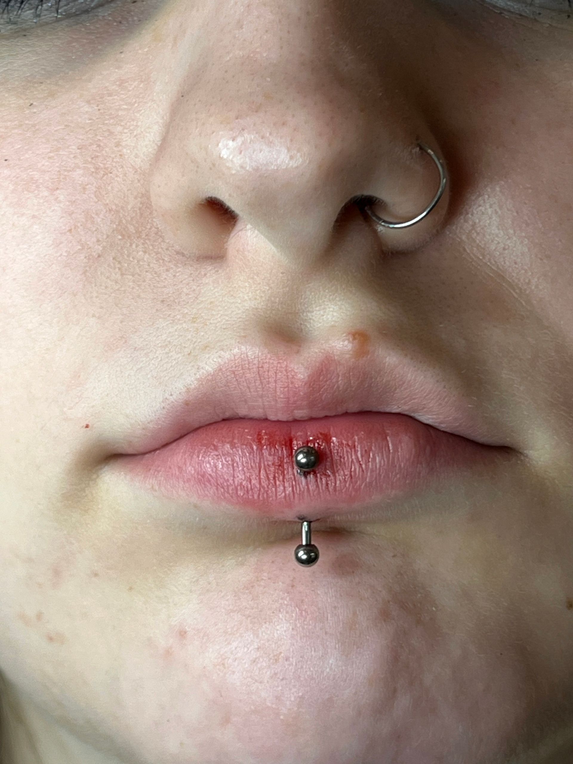 Een close-up van een centrale verticale labretpiercing op de onderlip, met een zilveren staafje met twee metalen kraaltjes.