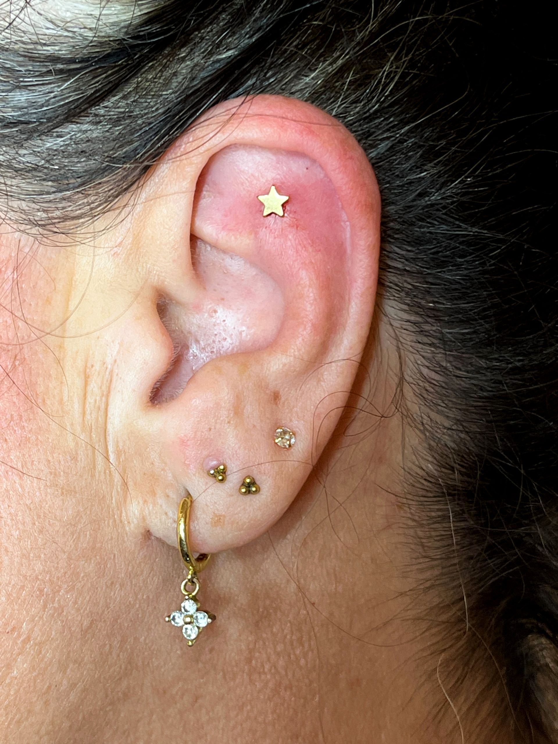 Een plat piercinggaatje in de vorm van een gouden sterretje in het bovenste deel van het oorkraakbeen, met drie gouden oorbeltjes en een klein hangend bedeltje.