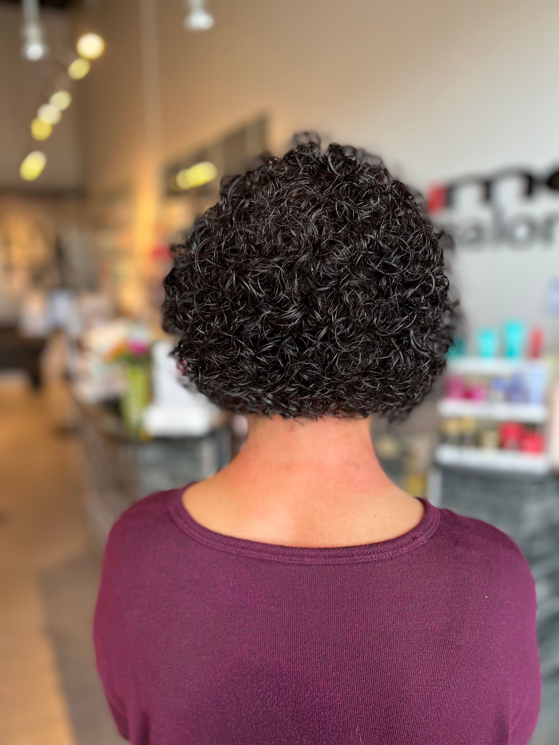 The back of a woman with curly hair wearing a purple sweater.