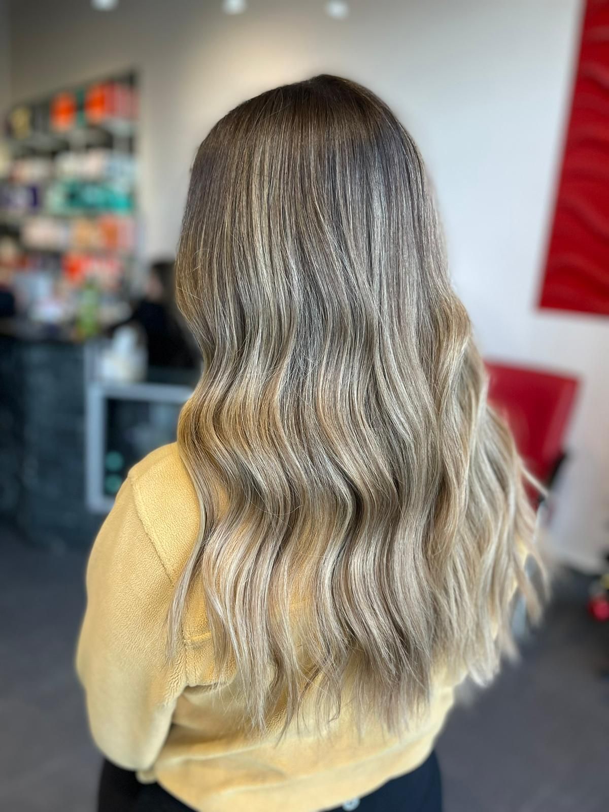 The woman is wearing a yellow sweater and has long wavy hair.