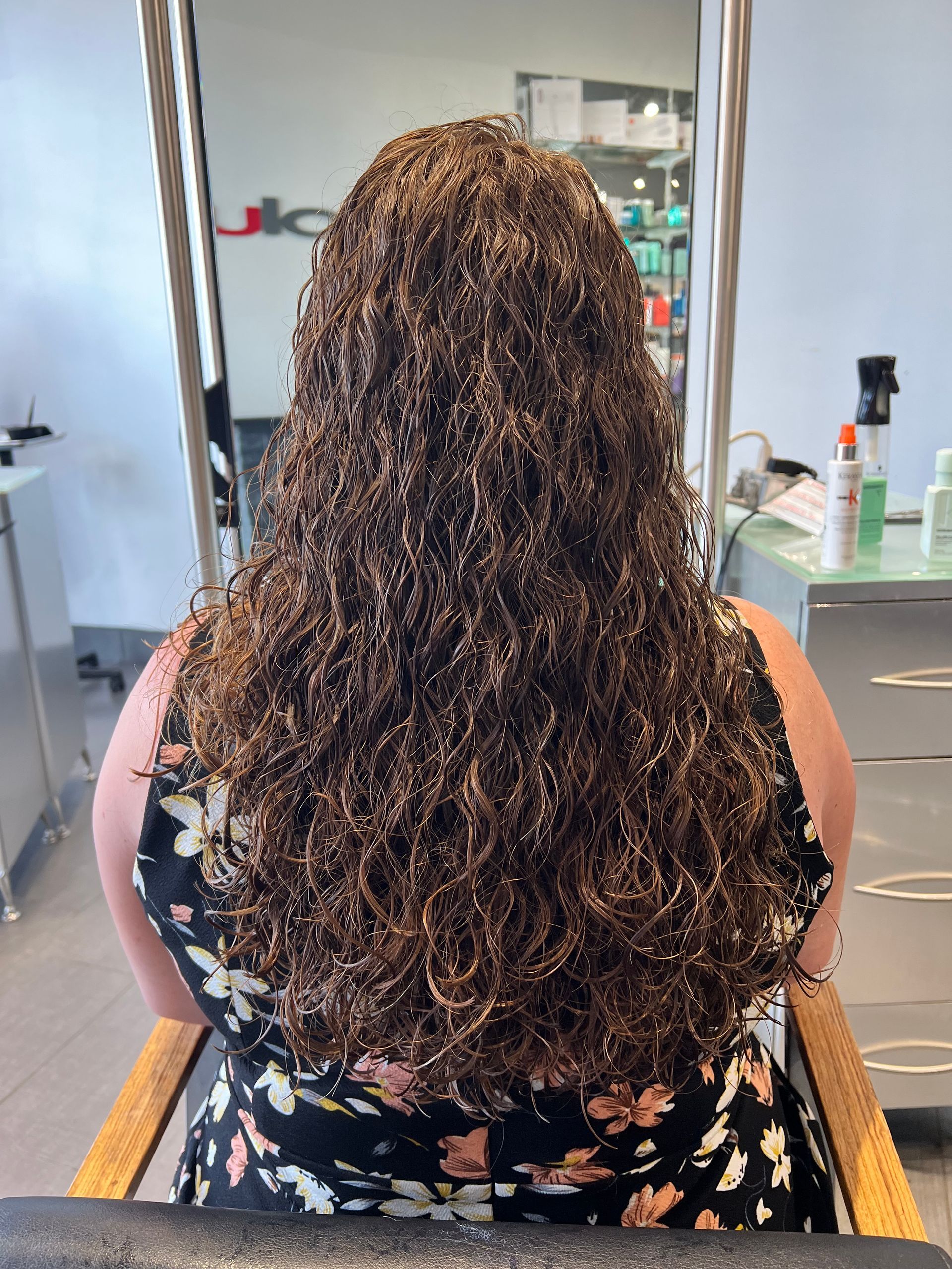A woman with long curly hair is sitting in a chair in a salon.