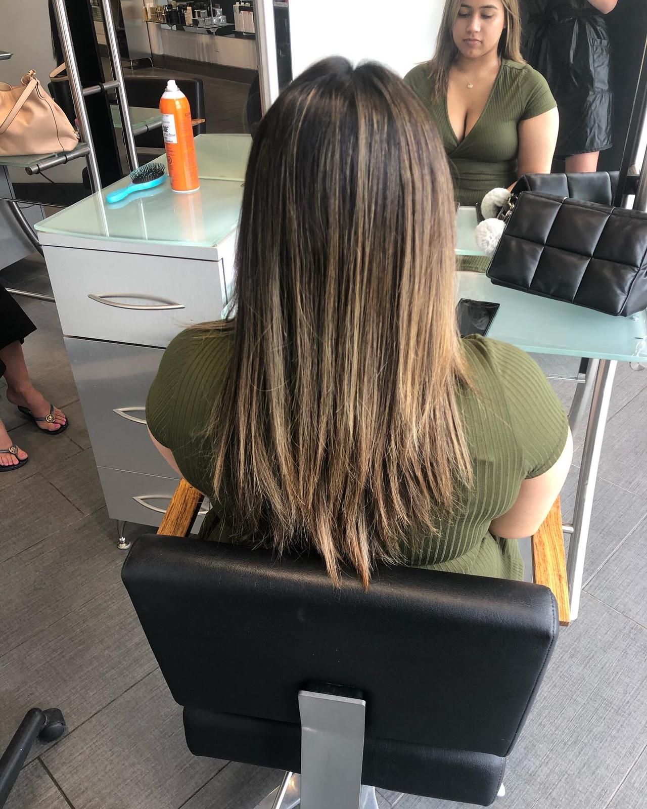 A woman is sitting in a chair in front of a mirror in a salon.