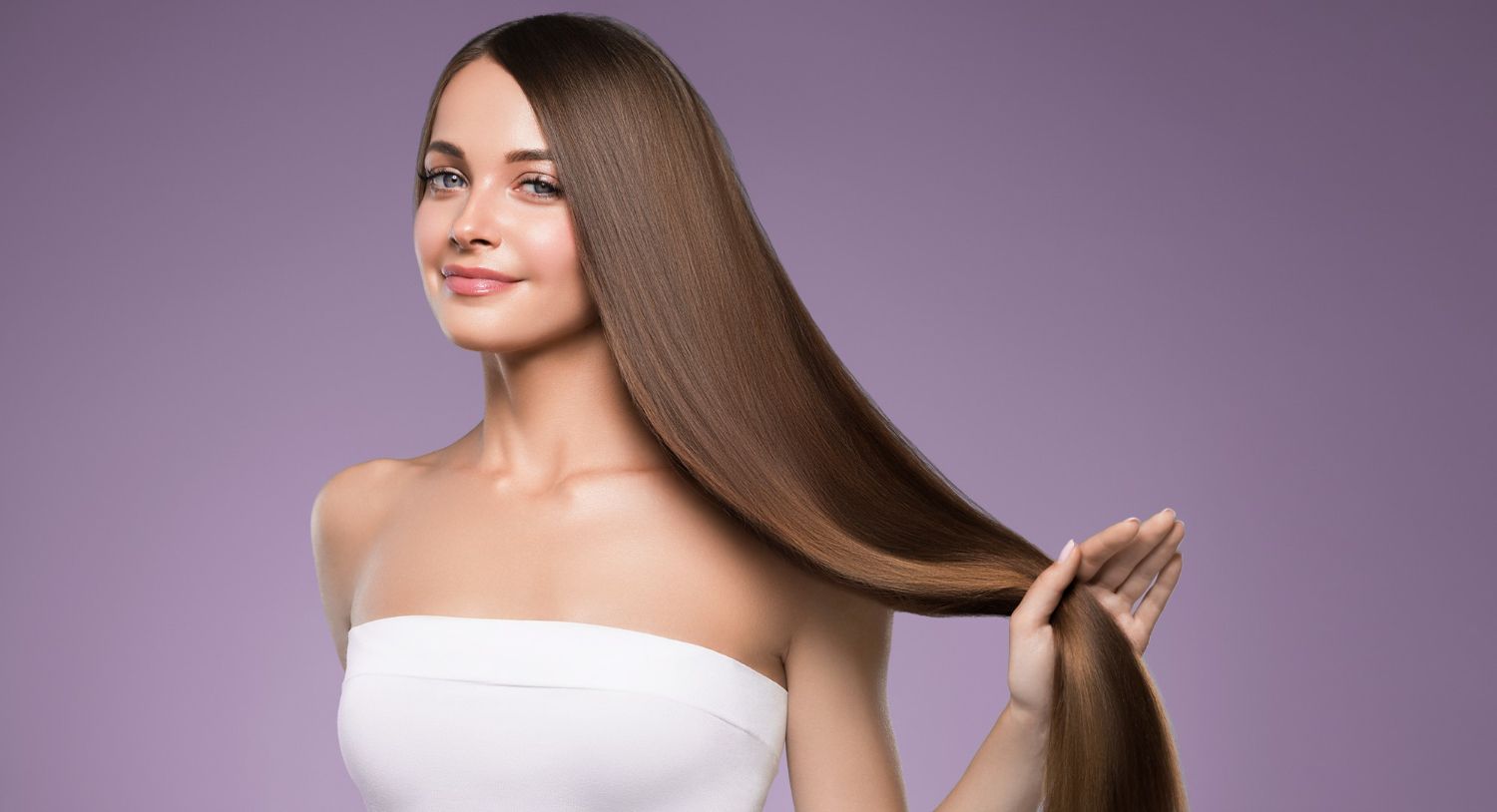 Woman with long brown hair against a purple background, holding a section of hair and smiling lightly