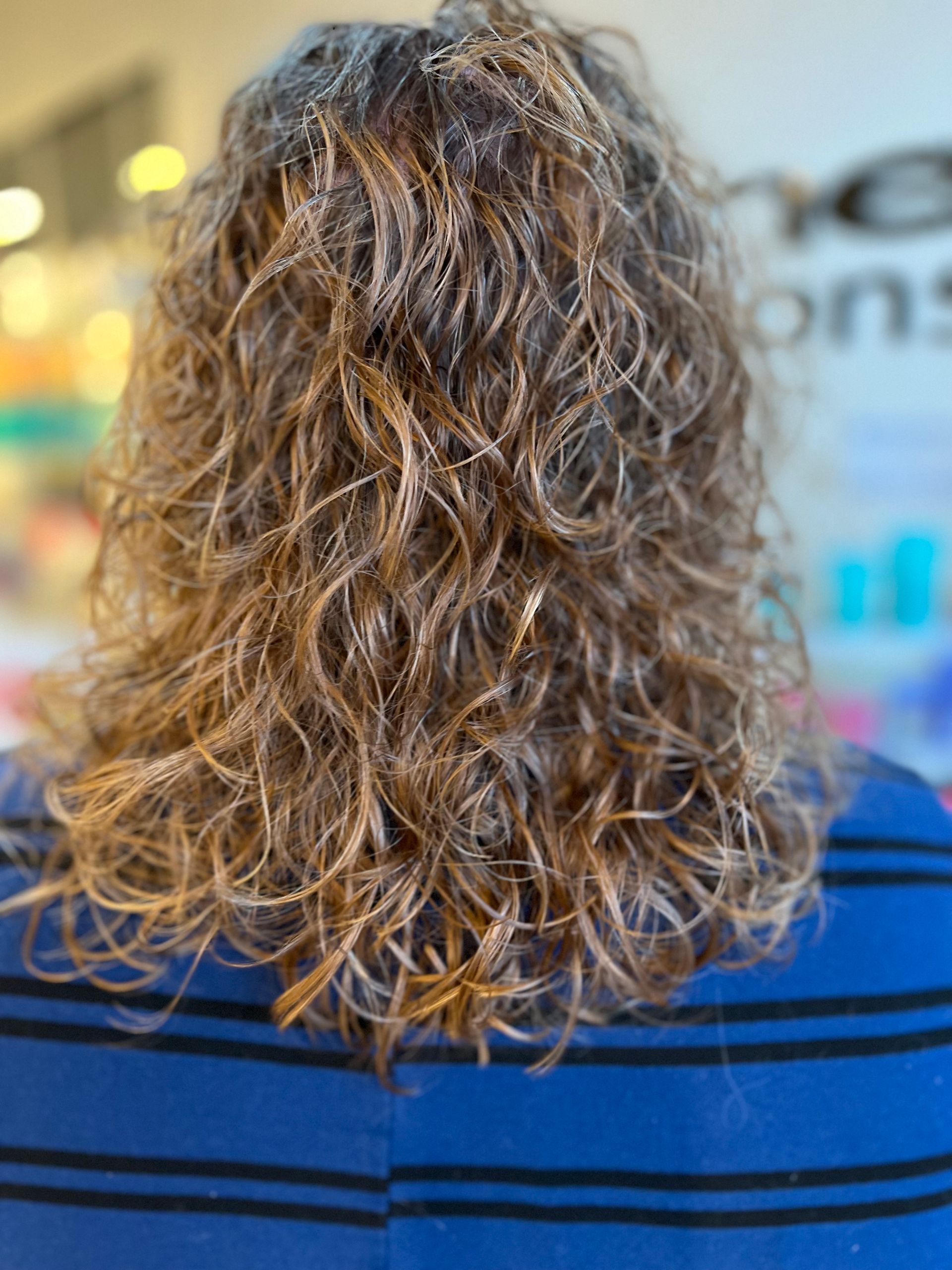 A woman with curly hair is wearing a blue striped shirt.