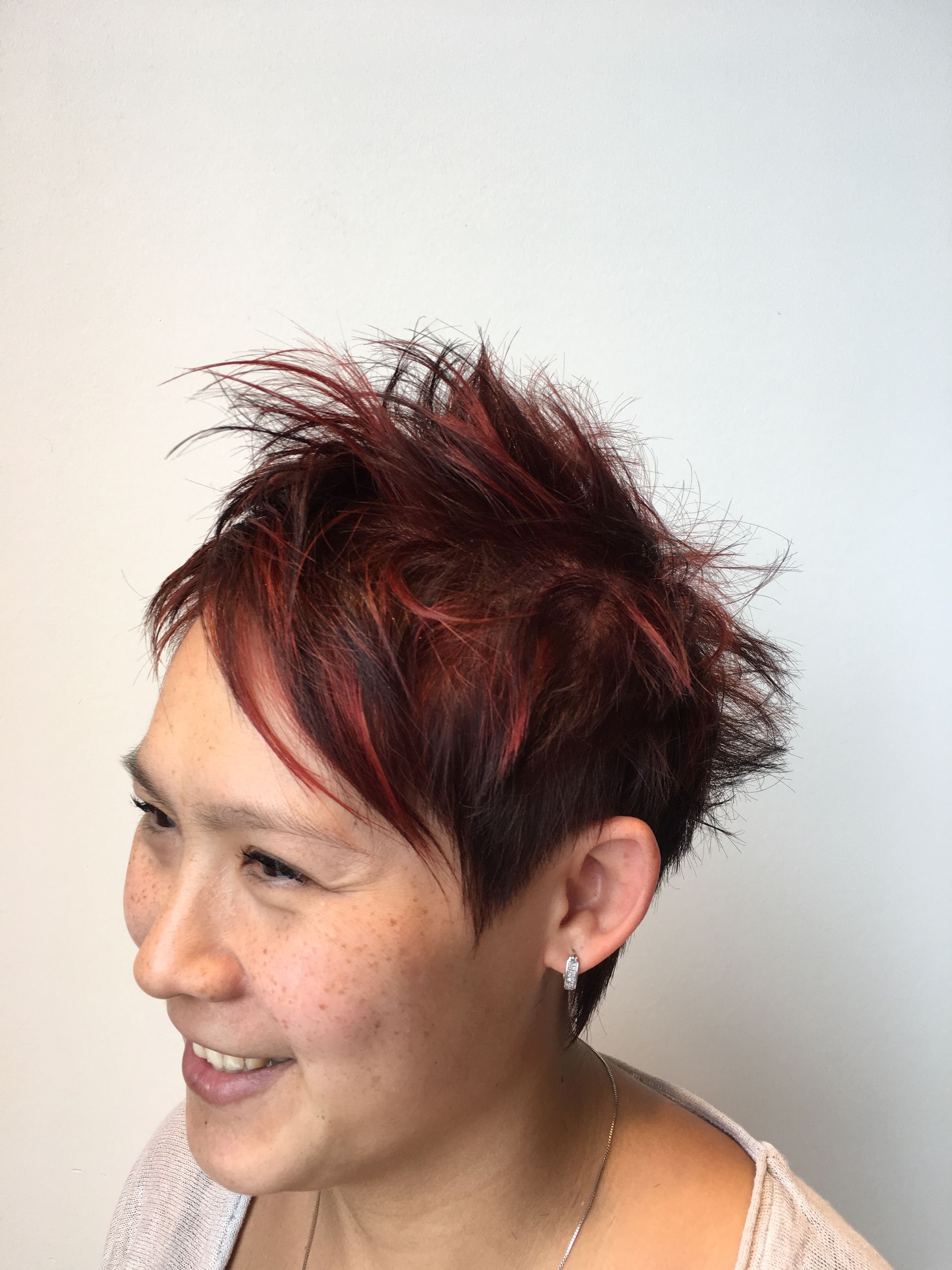 A woman with short red hair is smiling and wearing earrings.