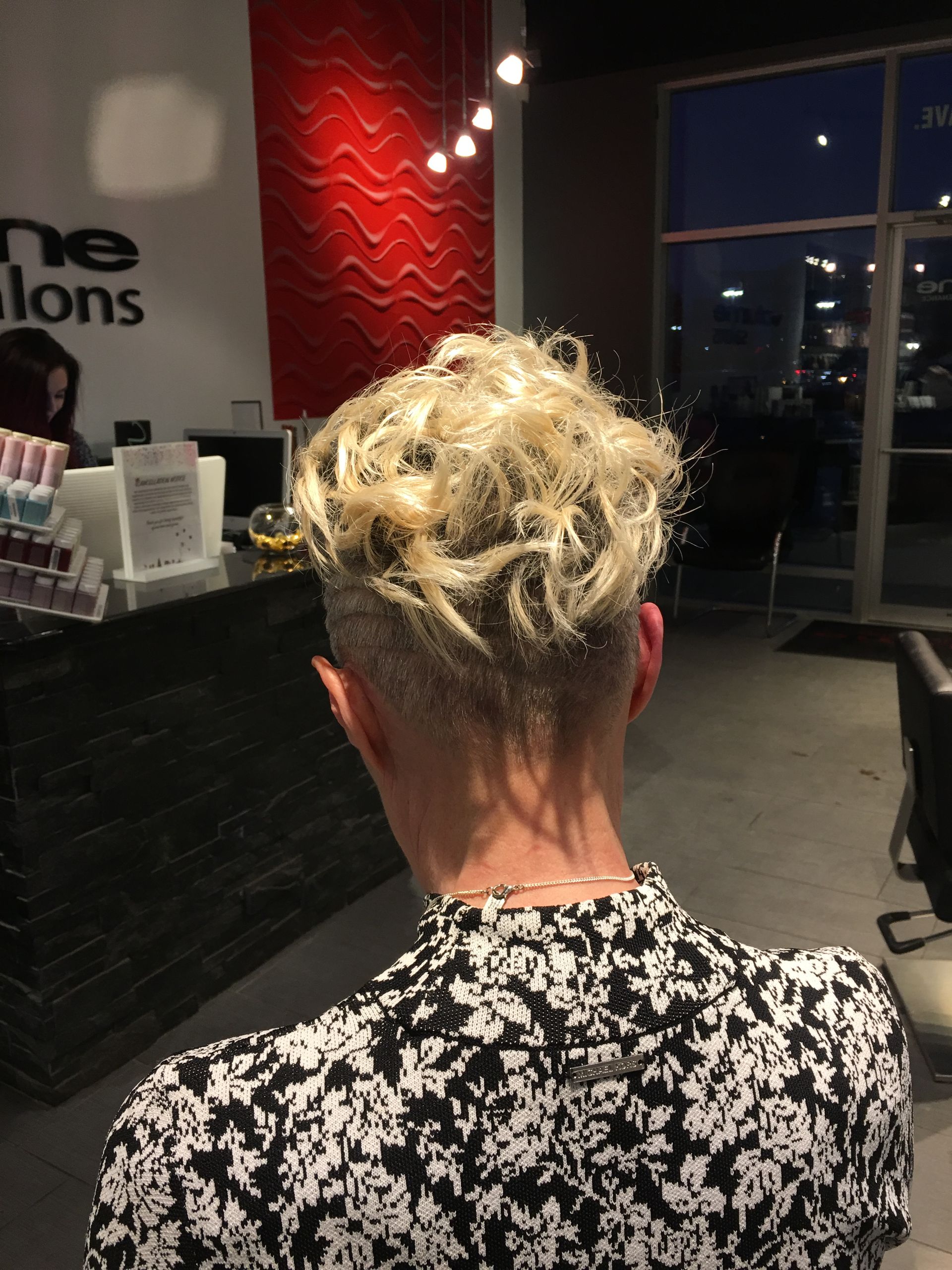 A woman with blonde hair and a shaved head is sitting in a salon.
