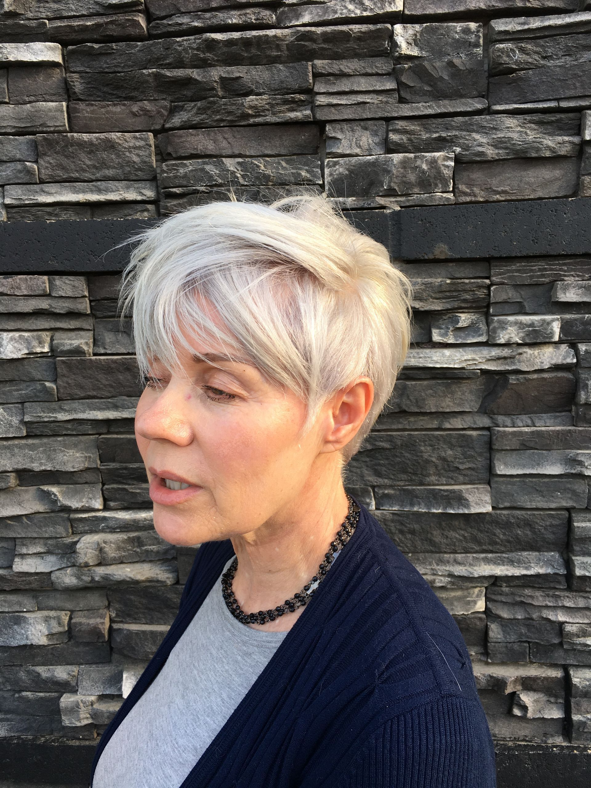 A woman with short gray hair is wearing a blue sweater and a necklace.