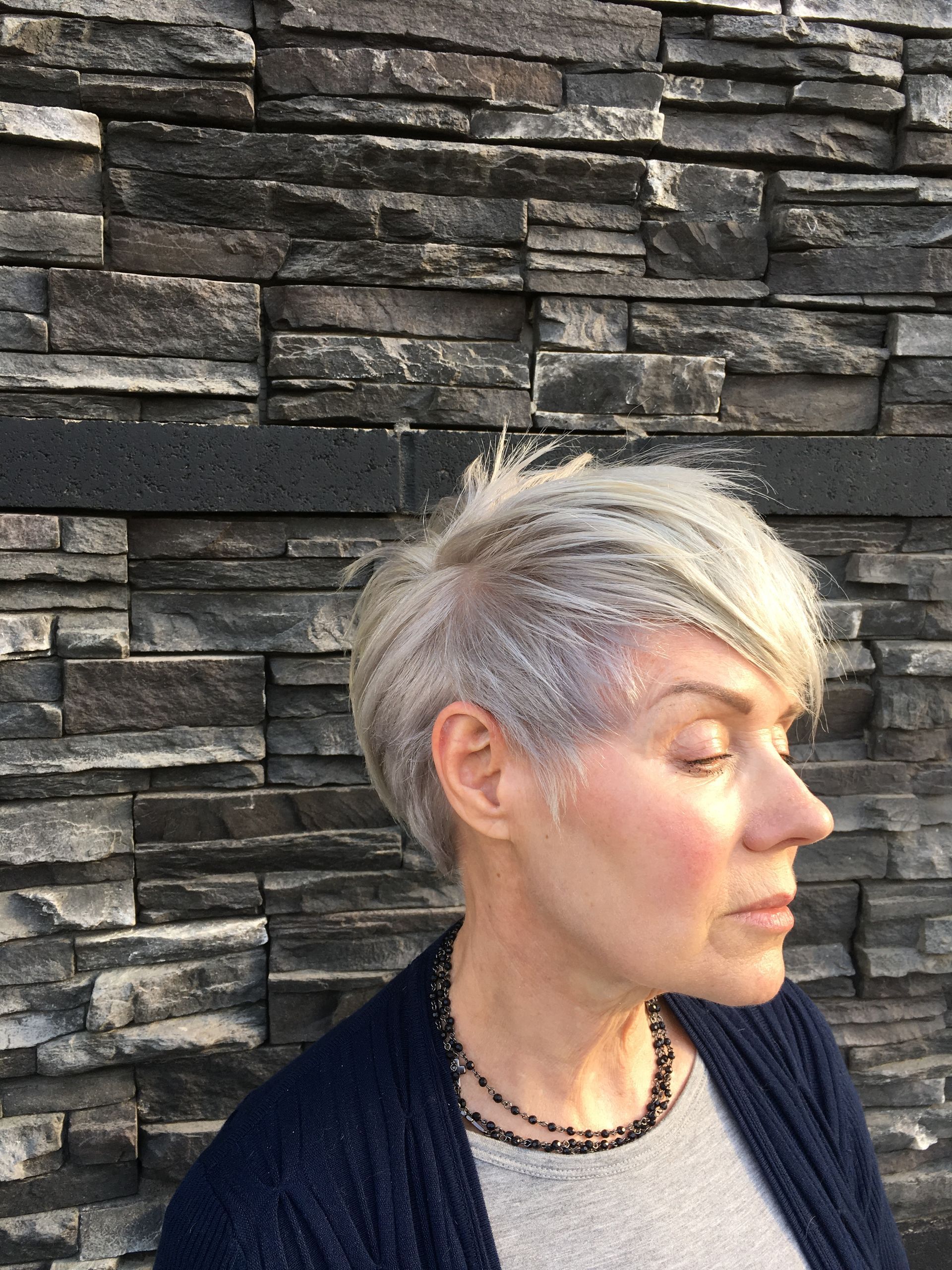 A woman with short blonde hair is standing in front of a stone wall.