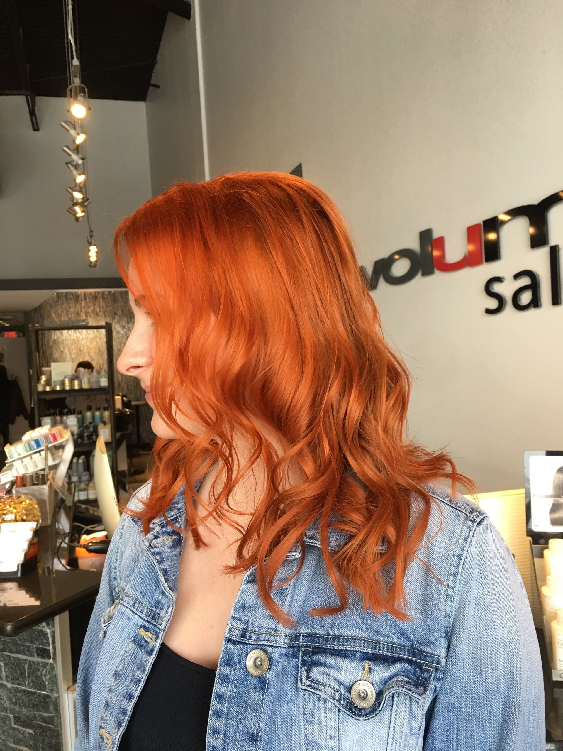 A woman with red hair is wearing a denim jacket in a salon.
