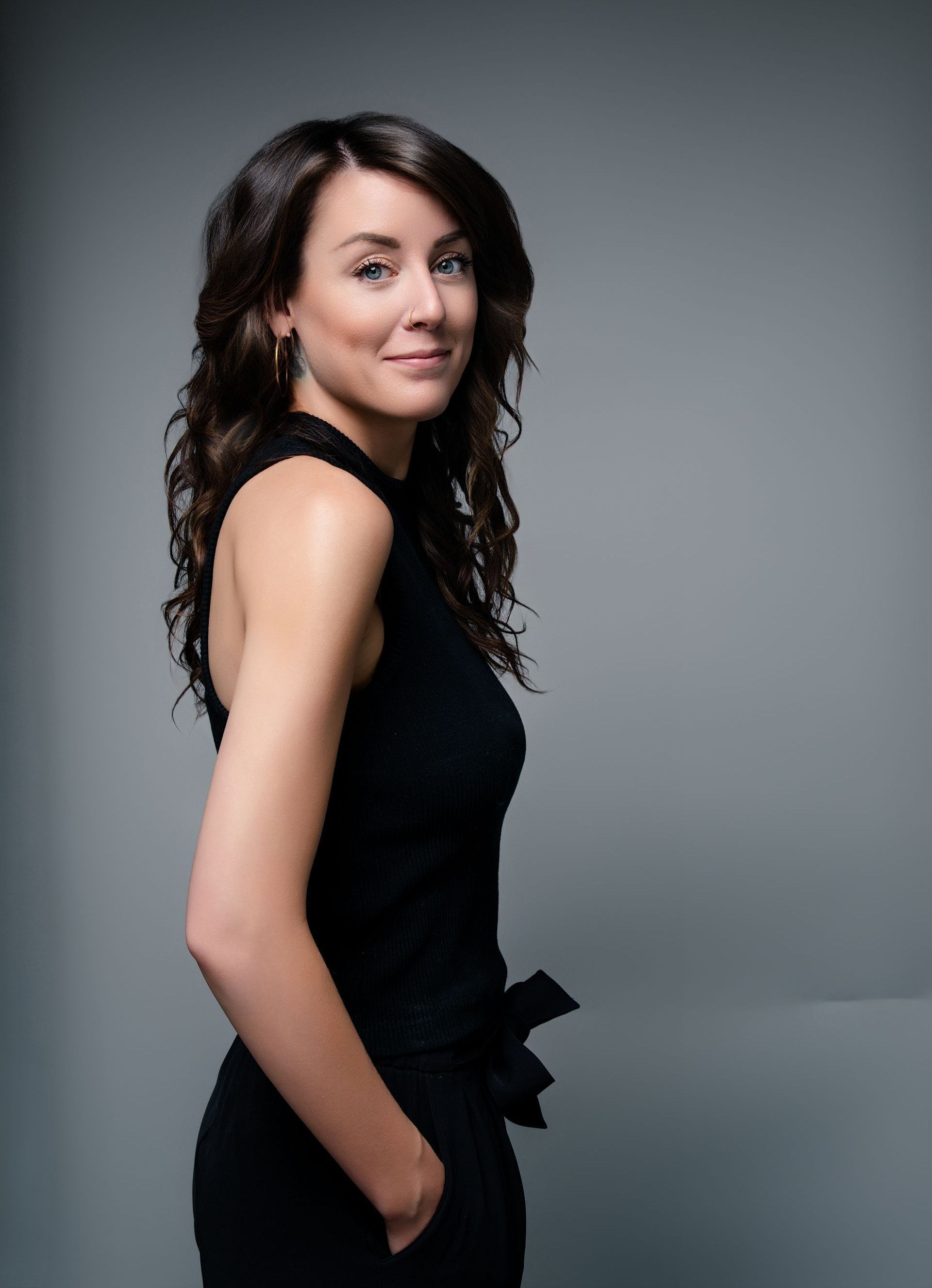 A woman in a black dress is standing with her hands in her pockets.