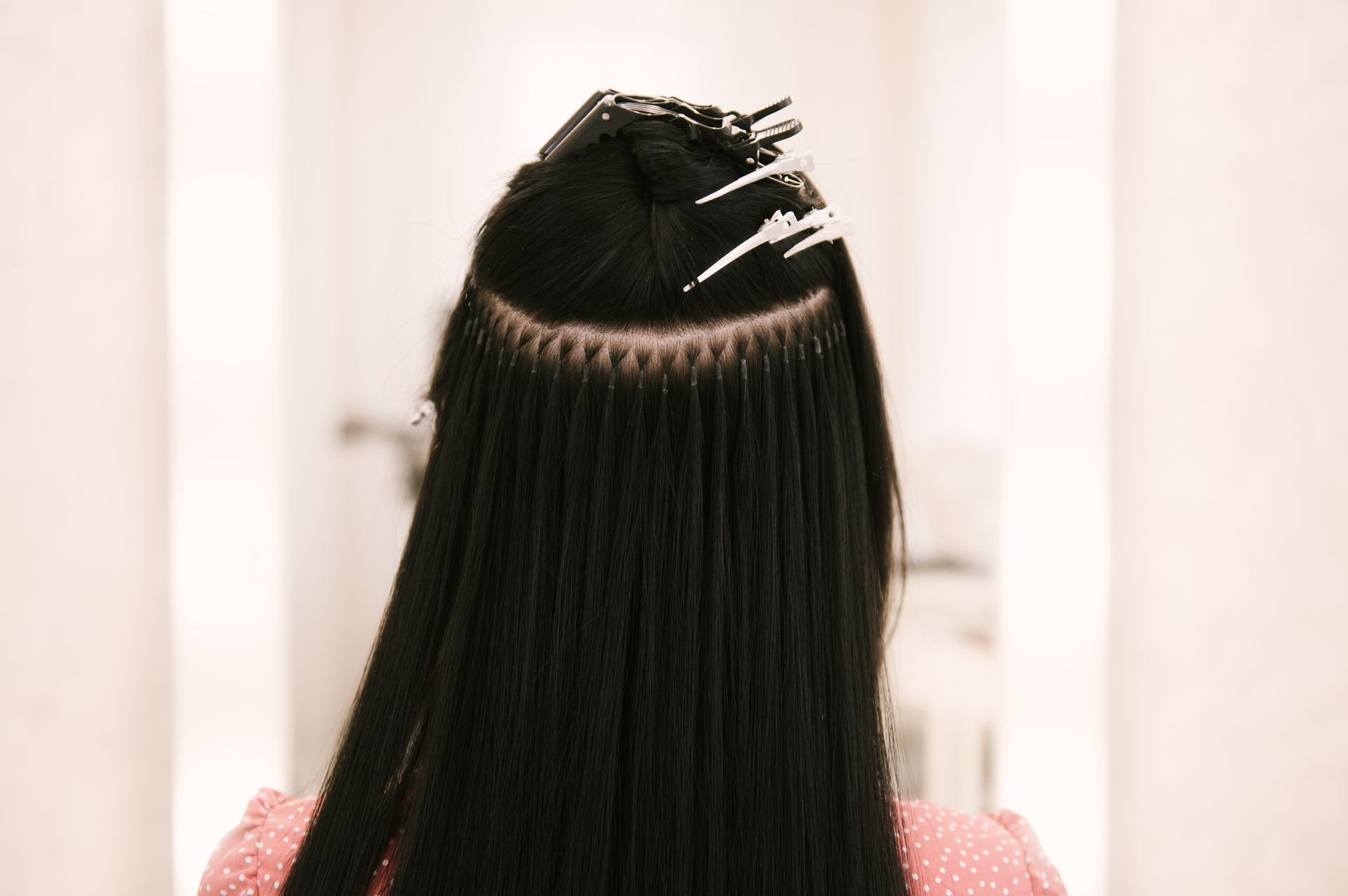 Hair extensions being braided onto dark straight hair, viewed from behind.