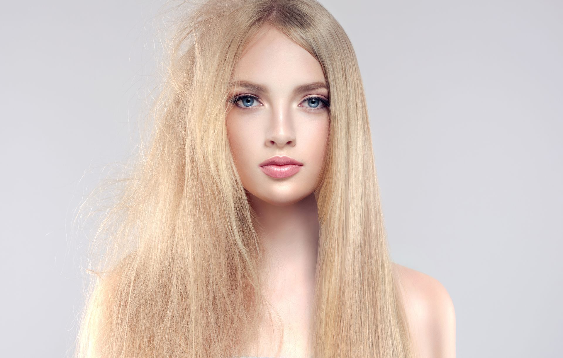 a woman with long blonde hair is standing in front of a gray background .