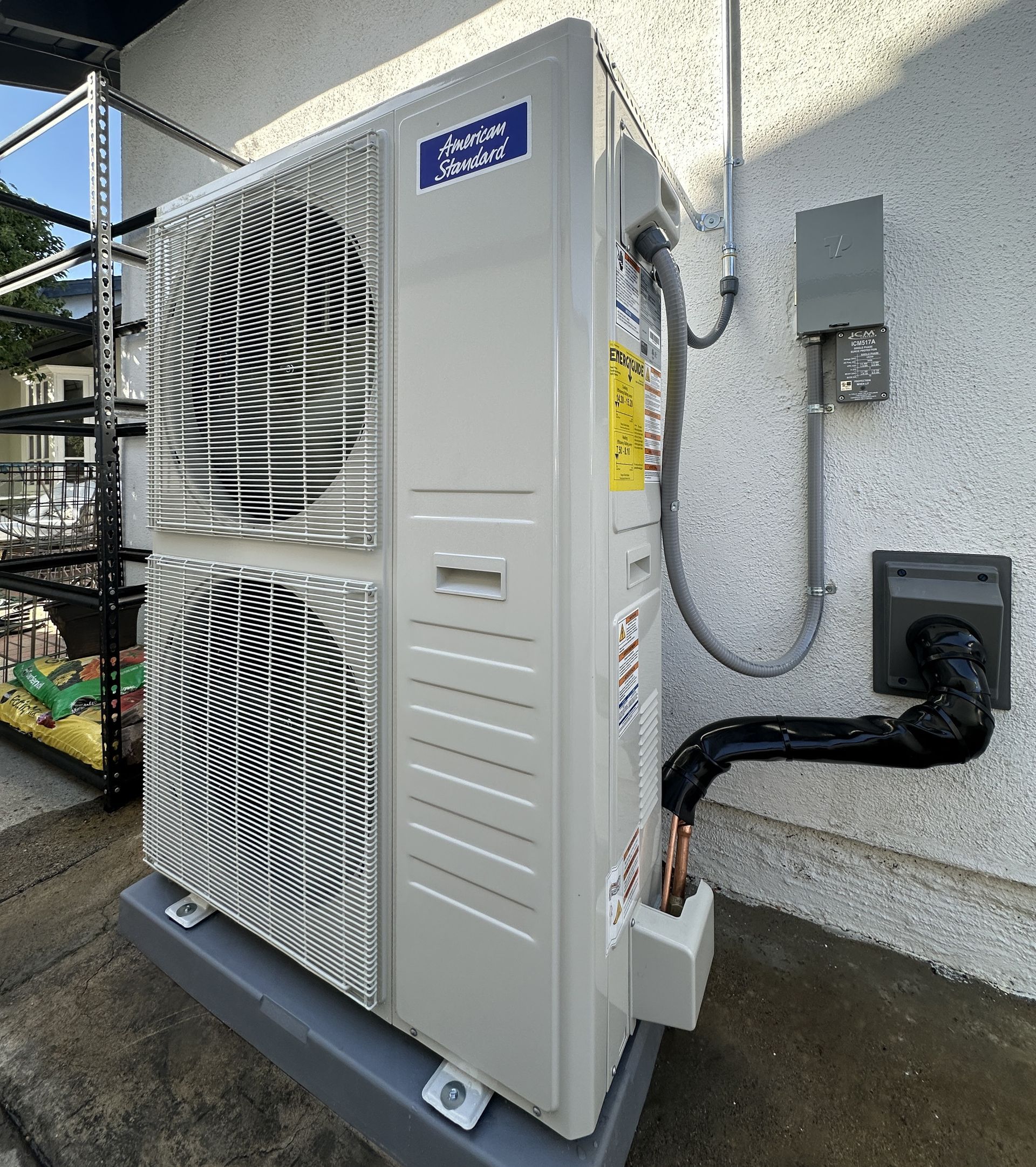 An outdoor air conditioning unit, light grey, mounted on a concrete pad next to a stucco wall.
