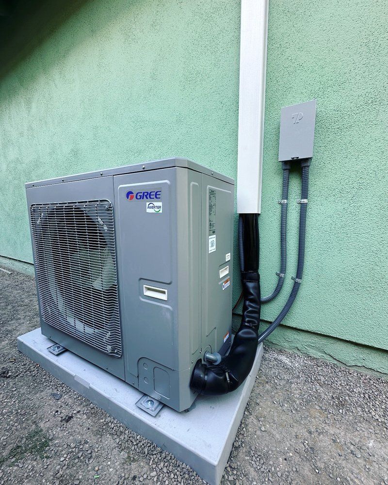 Tip of the Spear HVAC | a gray air conditioner is sitting on the side of a green building.