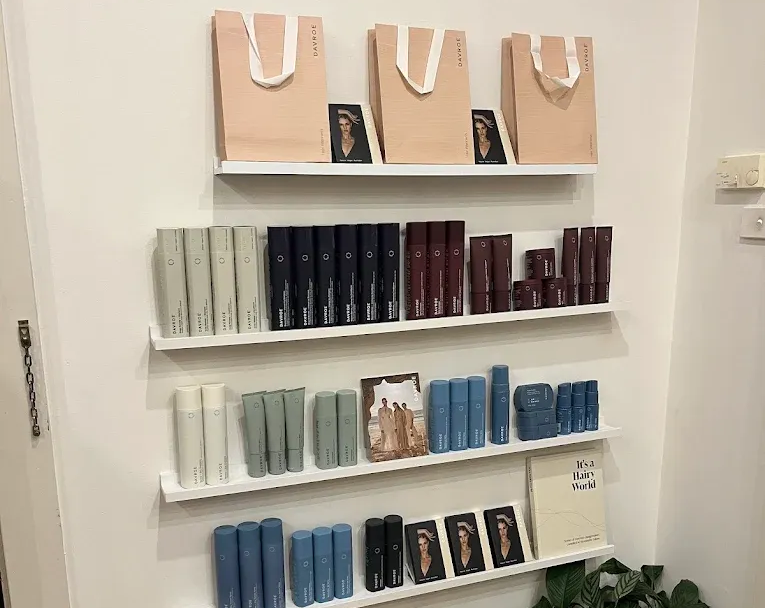 White wall with shelves displaying beauty products and gifts. Plant in corner.