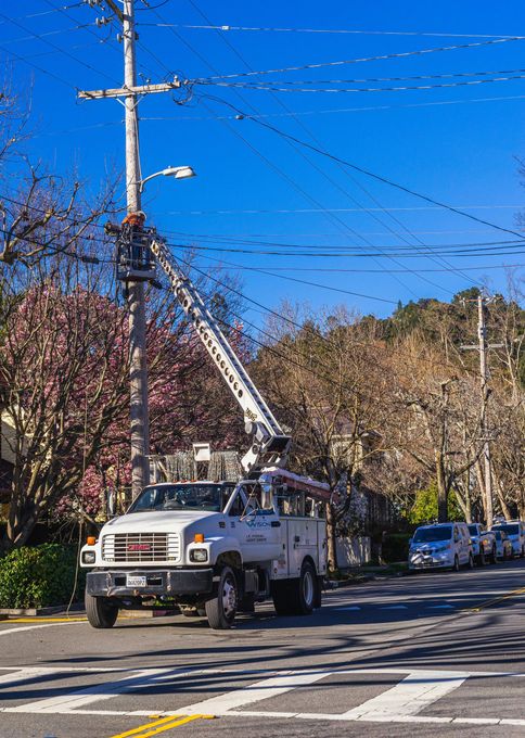 Utility truck with raised bucket near a power pole on a suburban street, under a bright blue sky