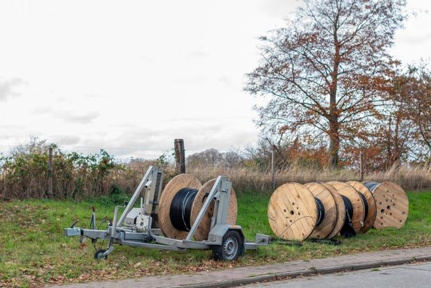 Wooden cable reel trailer beside stacked cable spools in a grassy field under cloudy sky