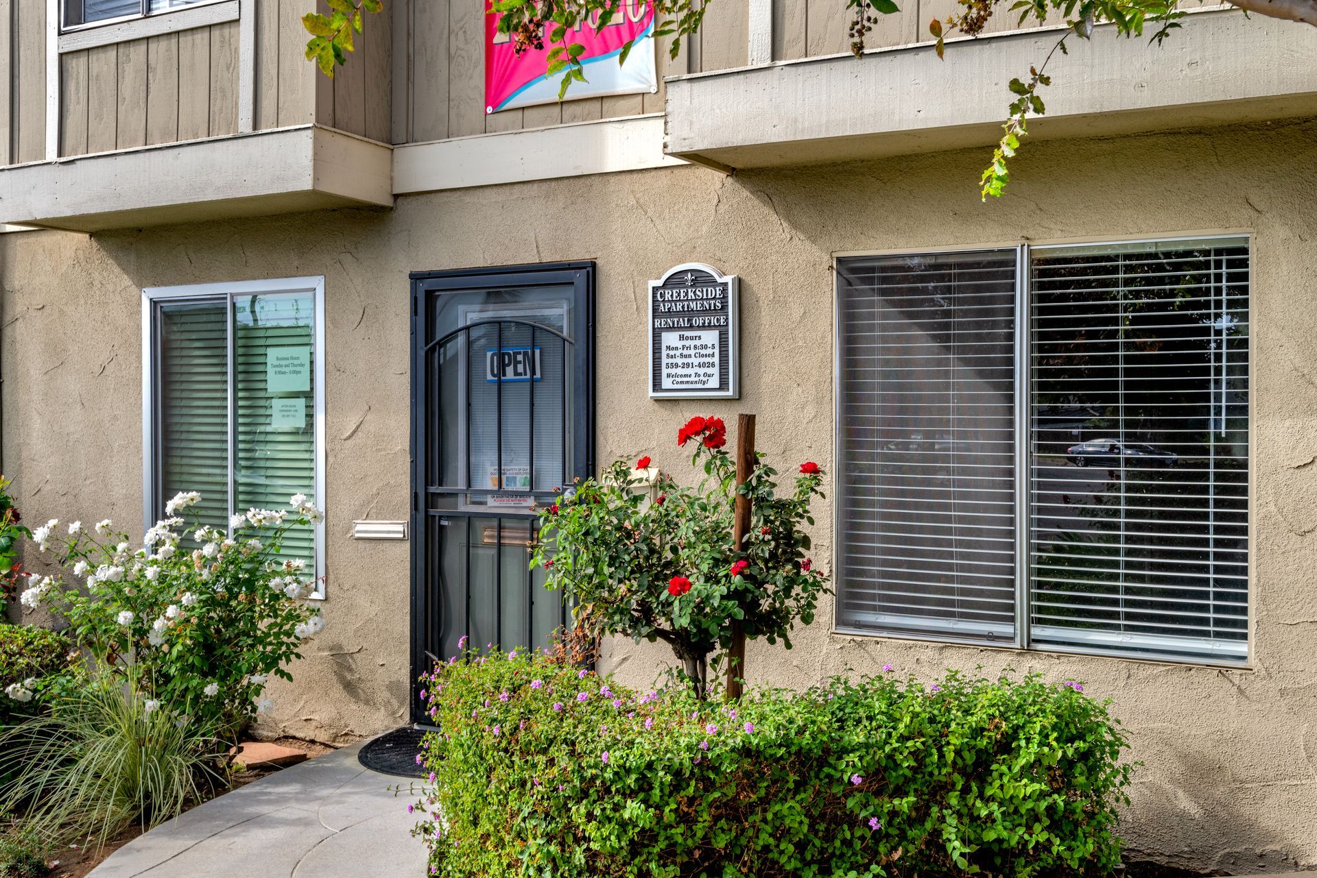 Exterior of a tan apartment building with a black door, windows, and landscaping.