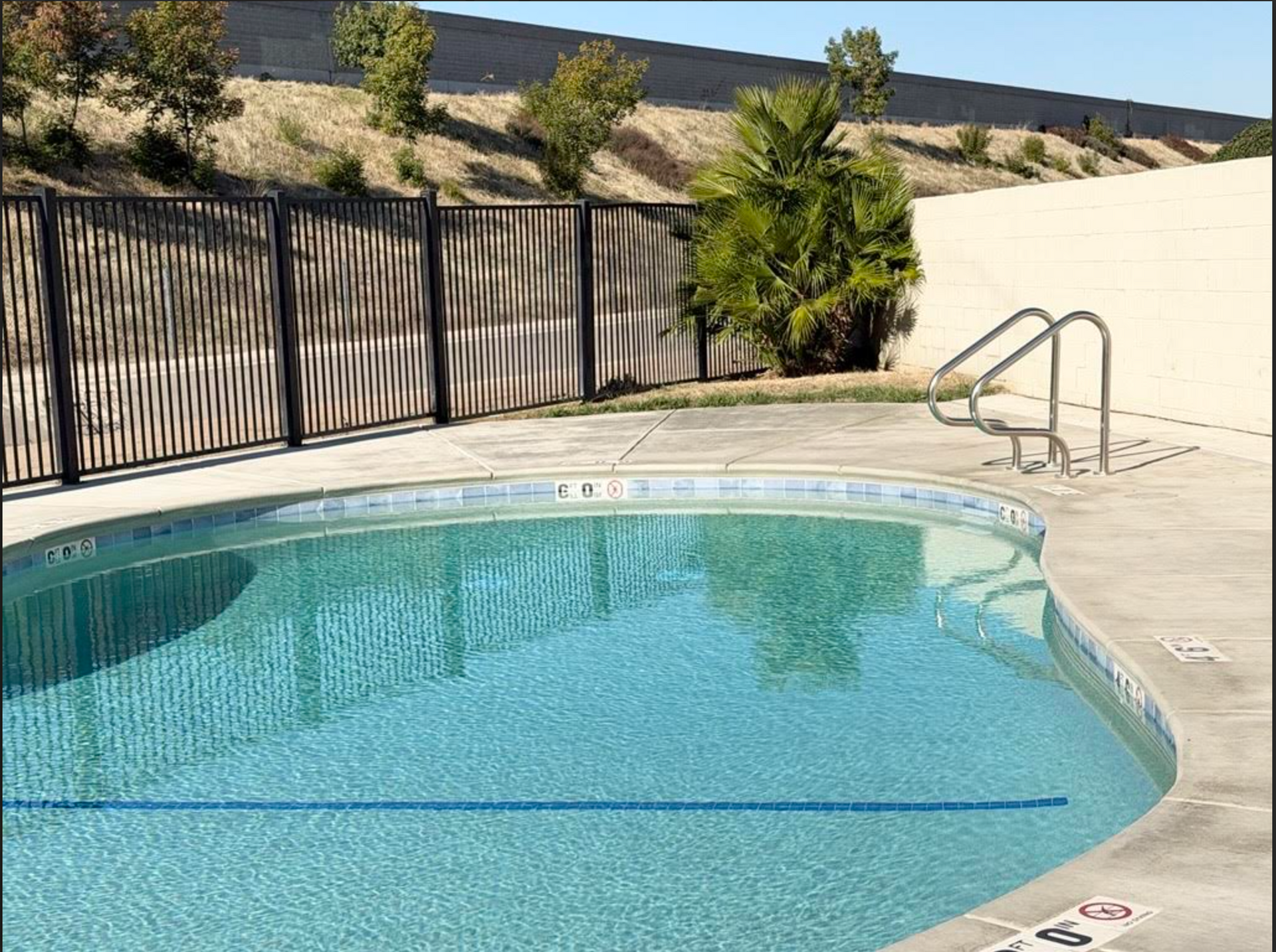 Pool area with table and chairs, enclosed by fences, blue sky, vehicle in background.