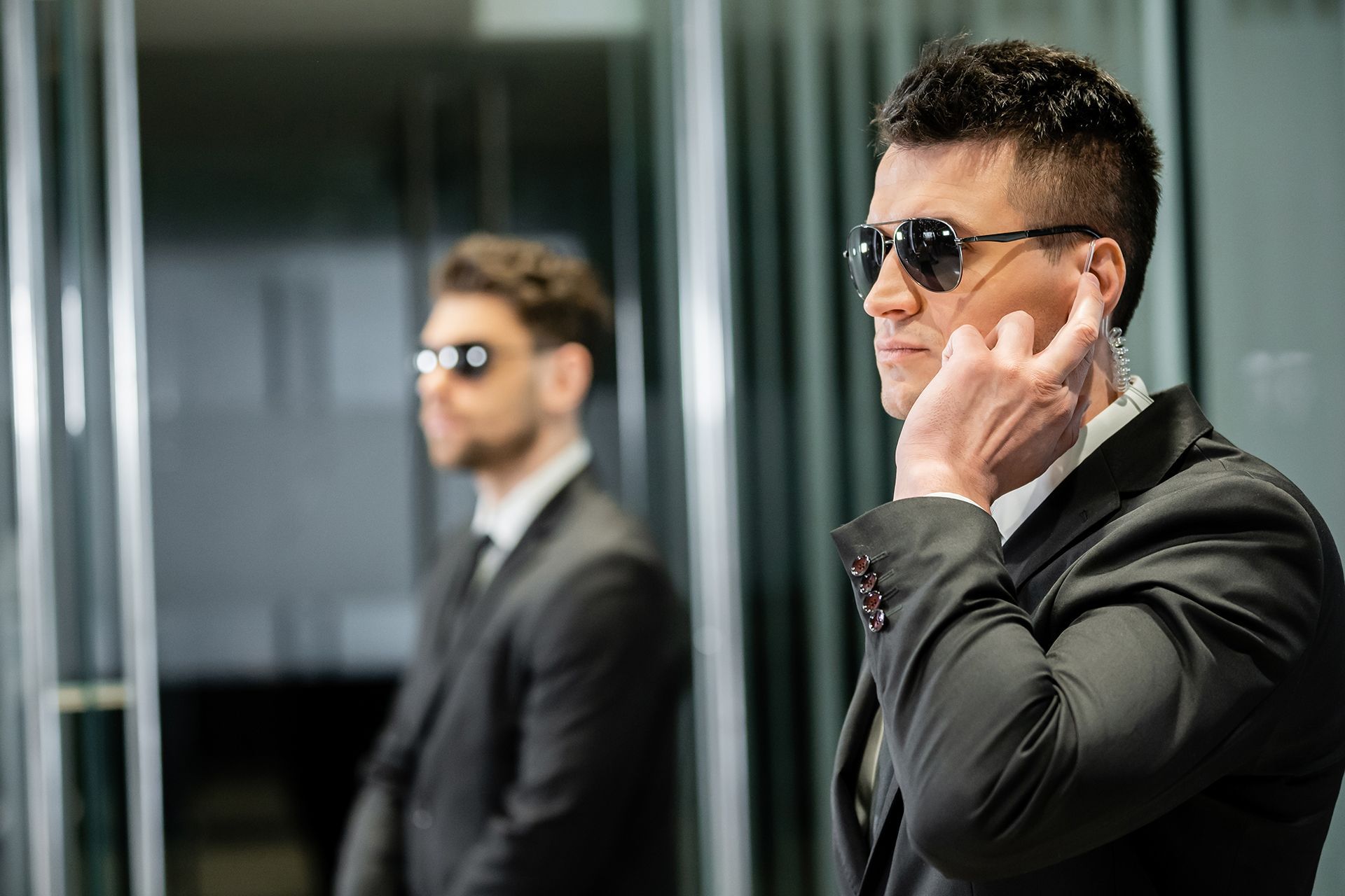 Two security guards wearing suits and sunglasses are standing next to each other.