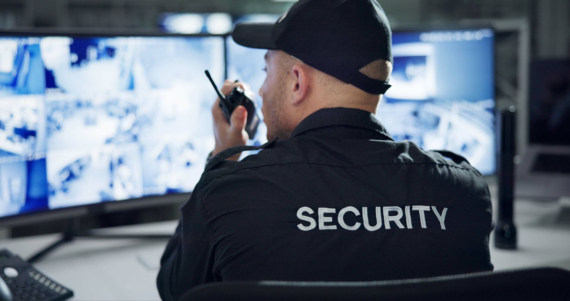 A security guard is sitting at a desk talking on a walkie talkie.