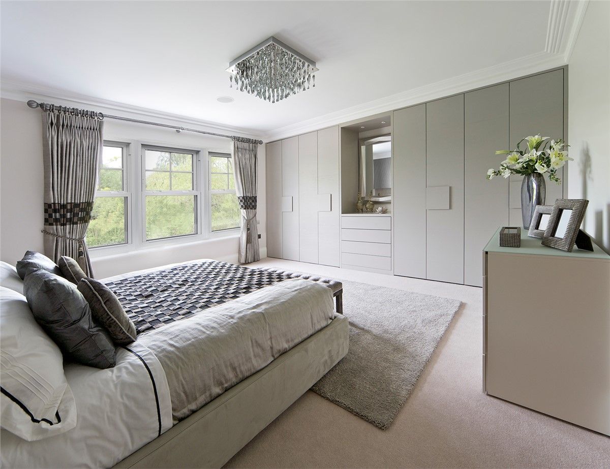 Bedroom with neutral tones, large bed, built-in wardrobe, window with curtains, and a small rug.
